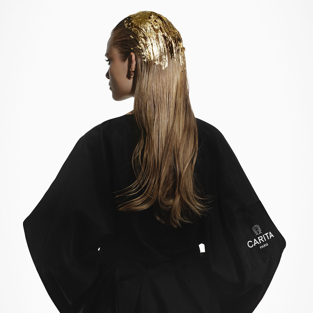 Donna bionda con foglie d'oro tra i capelli, che indossa un accappatoio nero Carita.