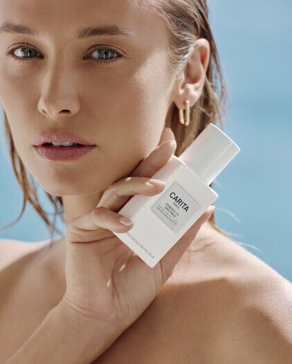 Primo piano di una donna che tiene in mano il flacone bianco di Essence UV.