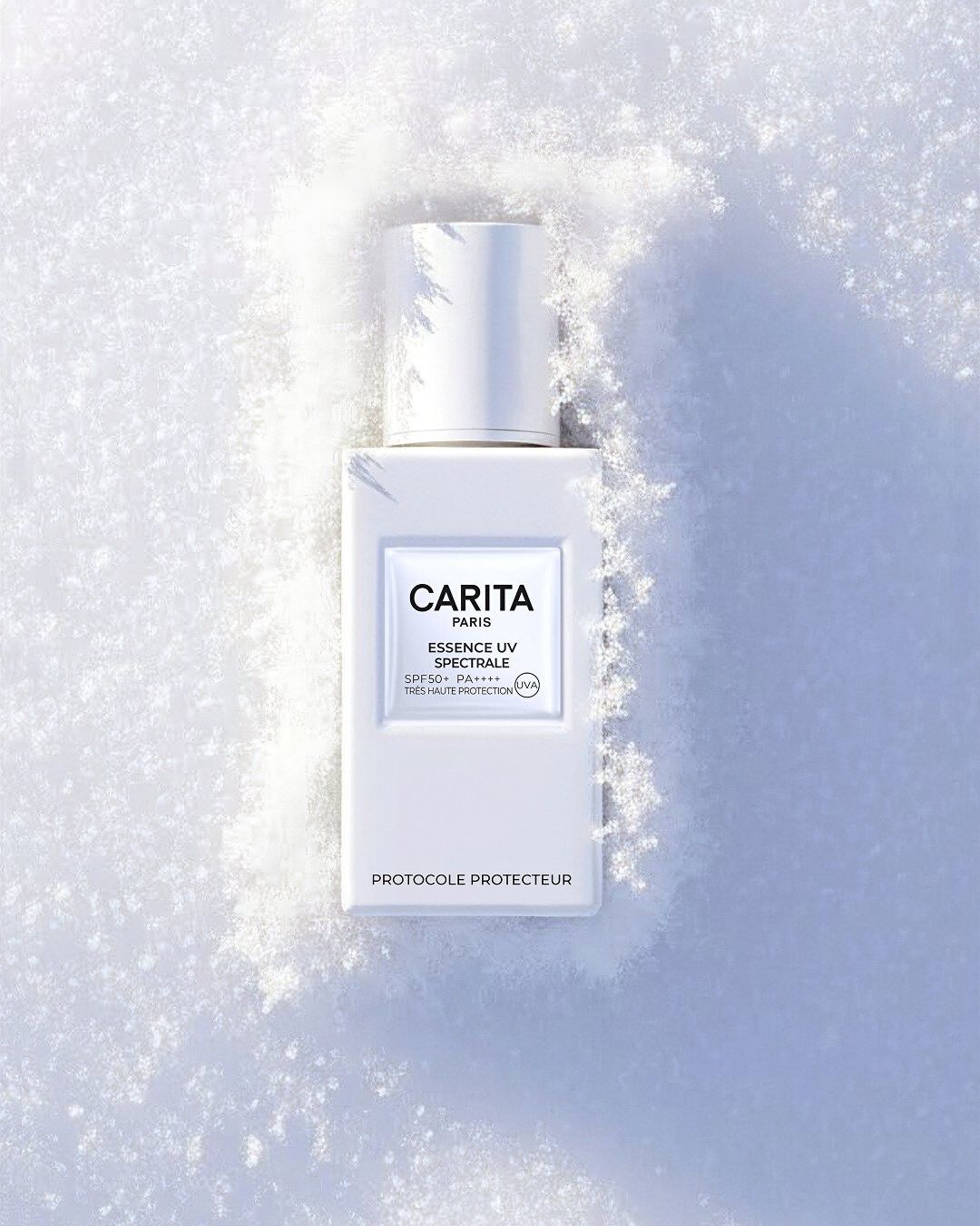 Veduta dall'alto del flacone bianco di Essence UV Spectrale Carita, adagiato nella neve. La luce radente mette in risalto la consistenza farinosa della neve e il design essenziale del prodotto.