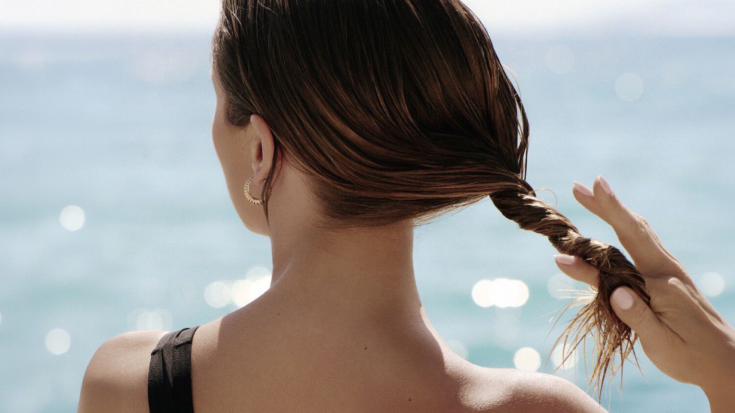 Una donna di spalle in riva al mare che si passa le mani tra i capelli.