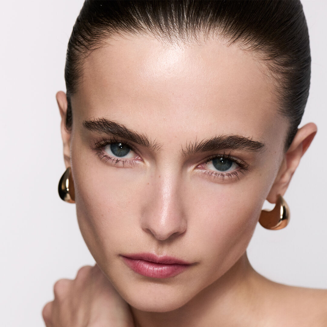 Donna mora con capelli effetto sleek e orecchini dorati.