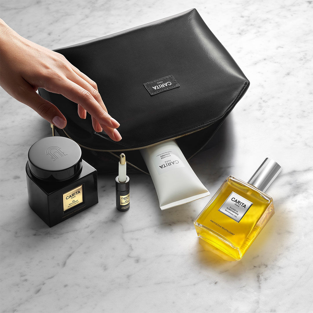 Prodotti di bellezza Carita e pochette nera su marmo.​