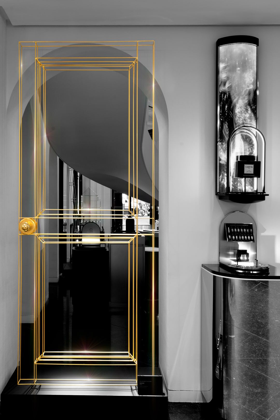 A stylized, transparent door frame outlined in gold is set against a monochromatic background in a modern interior space, featuring sleek furniture and decorative lighting.