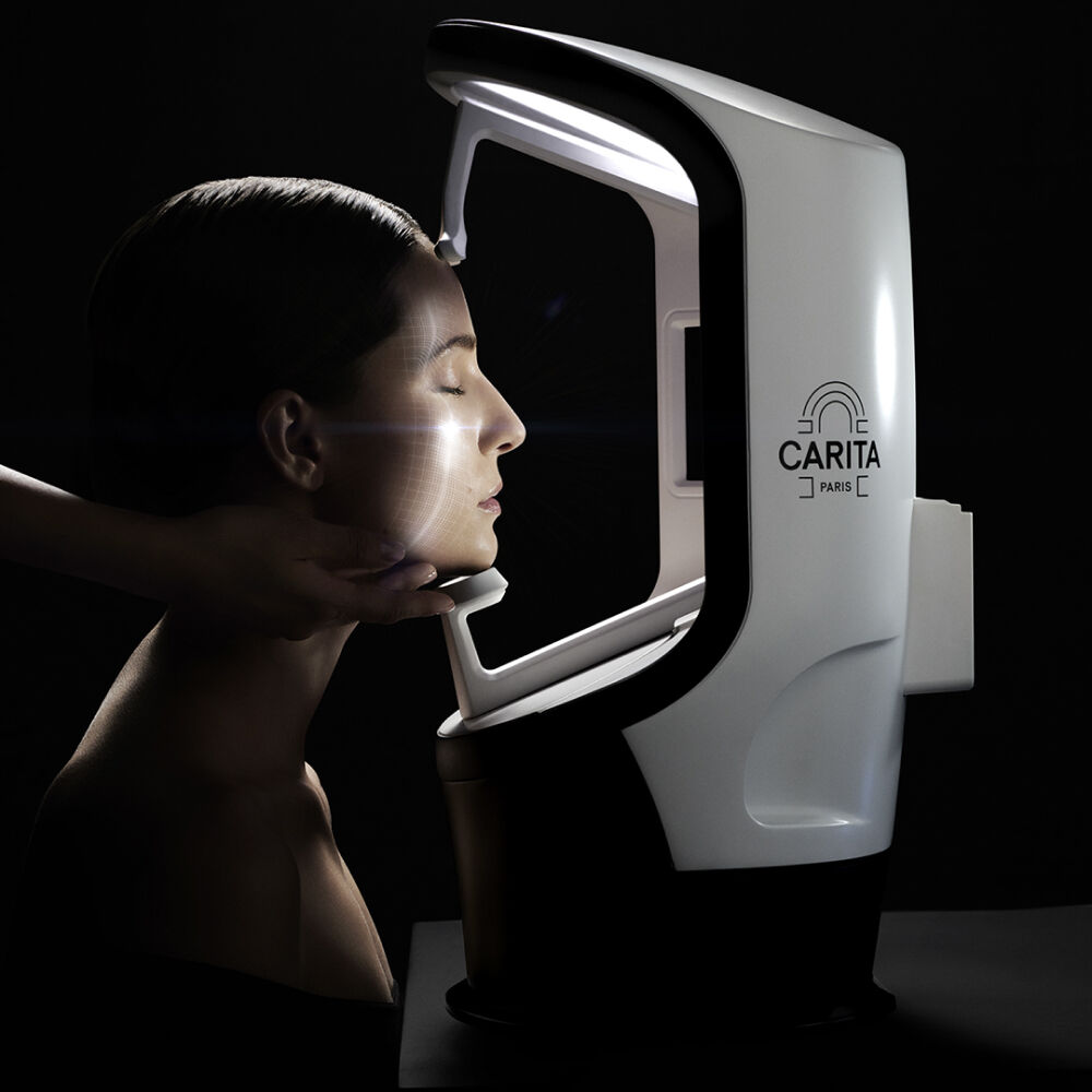 A close-up of a woman’s face in profile, illuminated by soft light, while a skincare device from Carita Paris is positioned beside her.