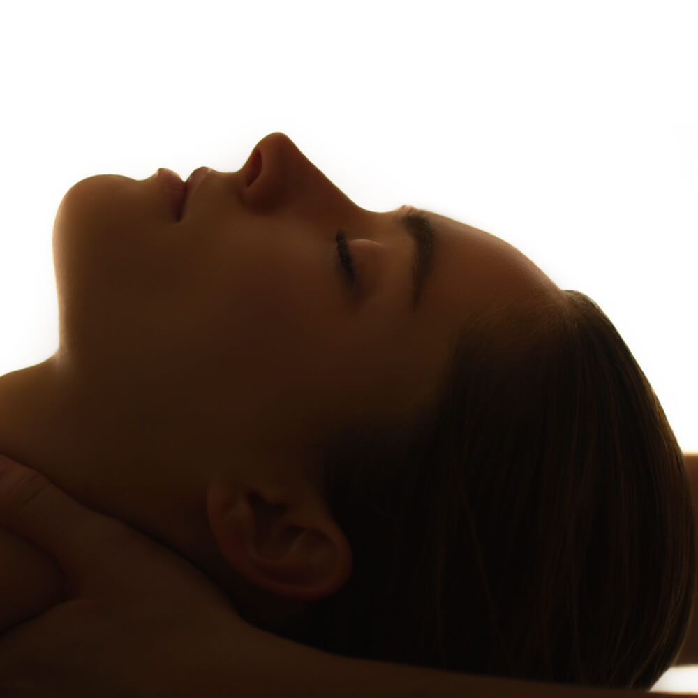 Primo piano del profilo di una persona con gli occhi chiusi e la testa reclinata all'indietro, illuminata da uno sfondo luminoso e diffuso. L'attenzione e focalizzata sulle sue espressioni serene e sui lineamenti delicati.