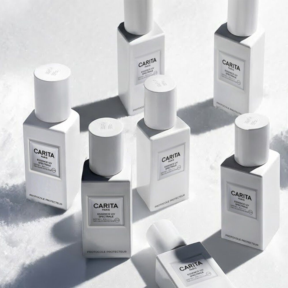 Diversi flaconi bianchi di Essence UV Spectrale Carita sono disposti artisticamente su una vasta distesa di neve immacolata.