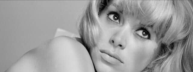 A close-up black and white portrait of a woman with blonde hair, looking thoughtfully to the side with a soft expression.