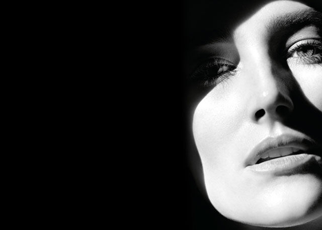A close-up of a woman's face in black and white, featuring dramatic lighting that highlights her features while casting shadows.