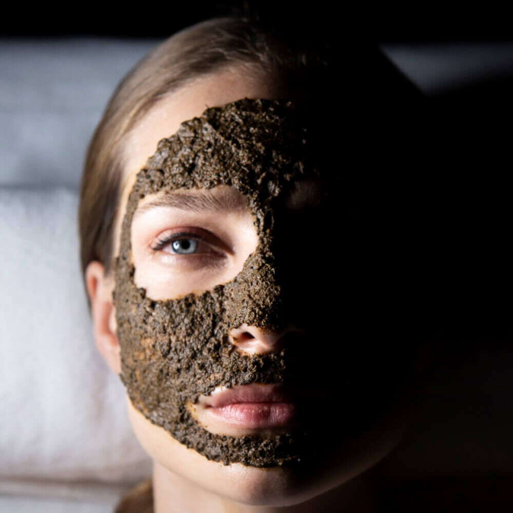 Primo piano di una donna con una maschera viso esfoliante scura.