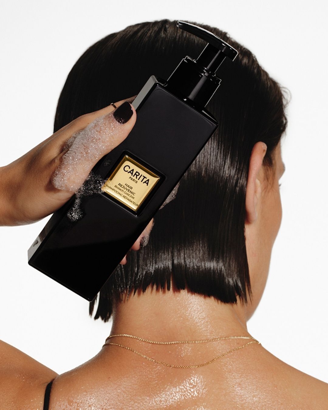 Donna con i capelli corti che tiene in mano lo shampoo riparatore Carita.