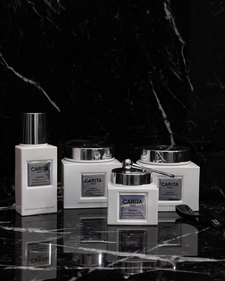 Prodotti per la cura della pelle Carita Paris "Cristal Morphologic" (creme, siero, applicatore) su marmo nero riflettente, evidenziando un protocollo di rimodellamento di lusso.