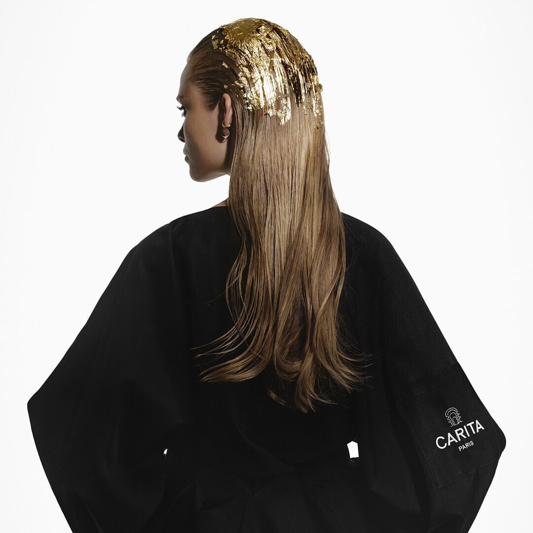 Donna bionda con foglie d oro tra i capelli, che indossa un accappatoio nero Carita.