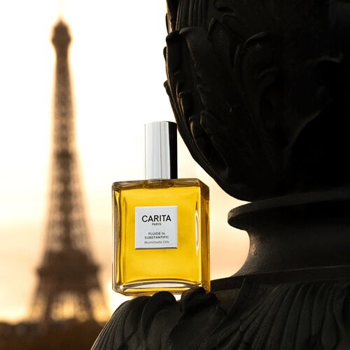 Vasetto di Carita Fluide 14 Substantific posato su un elemento architettonico scuro ed elegante, con la Torre Eiffel immersa nella luce dorata dell'alba o del tramonto sullo sfondo, evocando una sofisticata scena parigina.