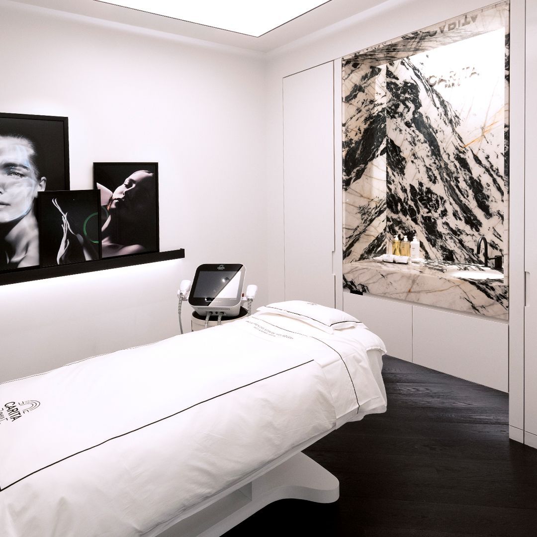 Moderna e lussuosa sala trattamenti con un letto bianco, un dispositivo estetico, una sorprendente decorazione murale in marmo bianco e nero e foto incorniciate.